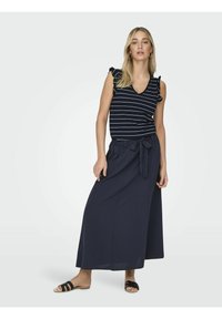 Top sans manches à rayures bleu marine avec des manches volantées, associé à une longue jupe bleu marine foncé avec un détail de taille nouée. Des sandales noires complètent le look.