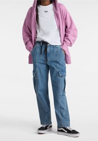 Lavendelkleurige hoodie, witte Vans t-shirt, blauwe cargobroek met zakken en zwarte Vans sneakers. De outfit heeft een ontspannen pasvorm en casual stijl.
