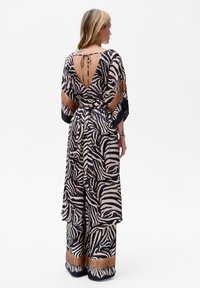 Maxi sukienka w zebrę z głębokim dekoltem na plecach, szerokimi rękawami i paskiem w talii. Wykonana w kolorach czarnym, beżowym i brązowym. Gładka struktura materiału.