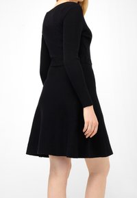 Svart tröjdress med lång, ribbad ärm, åtsittande bodice och utsvängd kjol, tillverkad av ett mjukt, texturerat tyg.