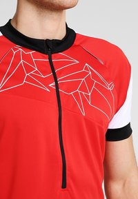 Camiseta deportiva roja con cremallera, que presenta acentos blancos en los hombros y un patrón geométrico blanco en la parte frontal. Tejido suave y ligero.