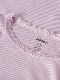 Šviesiai rožinė, ribb tipo audinys su banguotu nėrinių apykakle. Teksto etiketėje nurodyta dydžio ir prekės ženklo informacija. Minkšta tekstūra, paprastas dizainas.