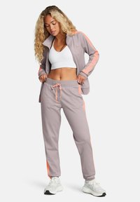 Sporta komplekts gaiši pelēkā krāsā ar korallkrāsas sānu akcentiem. Zipped jaka ar augstu apkakli un pieguļošas bikses ar regulējamu auklu jostasvietā.