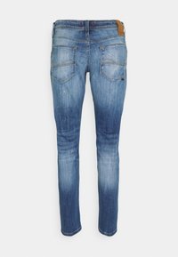 Siniset slim fit -farkut, joissa haalistettu pesu, hillityt kulutetut yksityiskohdat ja kaksi takataskua. Mukana ruskean sävyinen nahkainen takalappu.