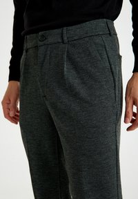 Grijze broek met een visgraatpatroon, gemaakt van gestructureerde stof, met knoopsluiting en zijzakken, weergegeven van de taille naar beneden op een model.