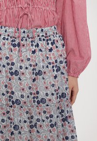 Rot-weißer gestreifter Oberteil mit Puffärmeln, kombiniert mit einem langen, gestuften Rock, der ein floralem Muster in Marineblau und Rosa auf einem hellen Hintergrund aufweist.