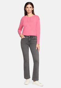 Różowy sweter z okrągłym dekoltem i sznurkami, w zestawieniu z szarymi prostymi dżinsami i białymi trampkami. Gładka tekstura, casualowy design.