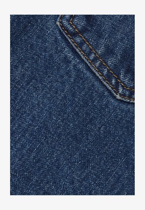 Sügavsinine denimkangas peene tekstuuriga kudumisega, millel on heledamad täpid ja kontrastne oranž õmblus taskute õmblustel.