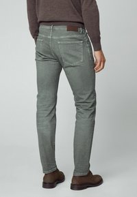 Jeans en denim gris à coupe slim, avec poches arrière et une étiquette en cuir marron sur la ceinture. La surface présente une texture lisse.