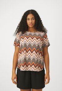 Top à manches courtes avec un motif zigzag multicolore en orange, noir et blanc. Tissu léger avec une coupe décontractée et un col rond.