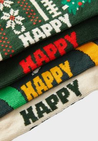 Drei gestrickte Weihnachtssocken in Grün, Rot, Gelb und Creme, mit dem Text "HAPPY" und festlichen Mustern mit Schneeflocken und Blättern.