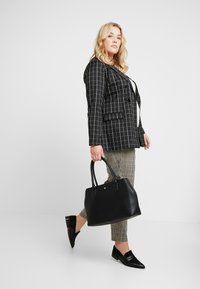 Blazer a scacchi neri, top crema e pantaloni a scacchi neri. Porta una borsa tote in pelle nera e indossa scarpe slip-on nere.