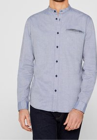Camicia a maniche lunghe in tessuto azzurro chiaro con un motivo sottile, colletto alla coreana e taschino sul petto. Presenta bottoni blu scuro e dettagli sui polsini.