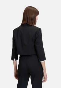Blazer nero corto con maniche a tre quarti, vestibilità sagomata e accenti bianchi a contrasto sulle maniche. Tessuto liscio e strutturato.