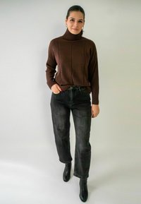Pull à col roulé marron à côtes, associé à un jean noir taille haute et des bottines noires. La tenue présente des détails en tricot texturé.