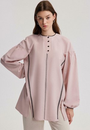 Roze blouse met lange mouwen en een ronde halslijn, zwarte knoopaccenten en zwarte stiksels langs de zijkanten, met geplooide mouwen.