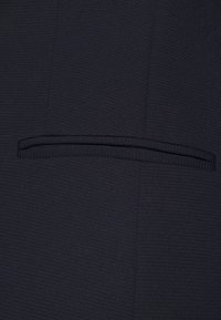 Tissu bleu marine foncé avec un motif texturé, comprenant une petite poche discrète intégrée dans le design du vêtement.