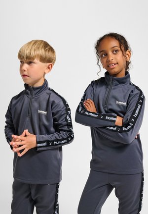 Grijze sportieve zip-up tops met lange mouwen, voorzien van zwarte zijstrepen en logo-accenten. Beide gecombineerd met bijpassende grijze onderstukken.
