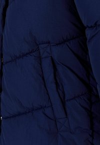 Tejido de chaqueta acolchada en azul marino con textura acolchada. Cuenta con un bolsillo lateral y costuras duraderas. Diseño ligero y aislante.