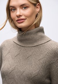Beżowy sweter wełniany z wysokim kołnierzem, z teksturowanym wzorem w diamenty i żeberkowym wykończeniem. Miękki materiał i luźny krój.