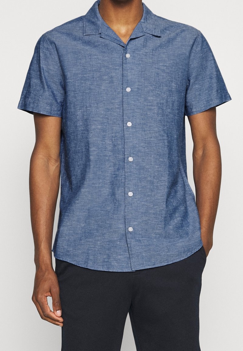 Camicia a maniche corte con bottoni, realizzata in un tessuto blu texture con colletto da campeggio, caratterizzata da una vestibilità leggermente rilassata e sei bottoni frontali.