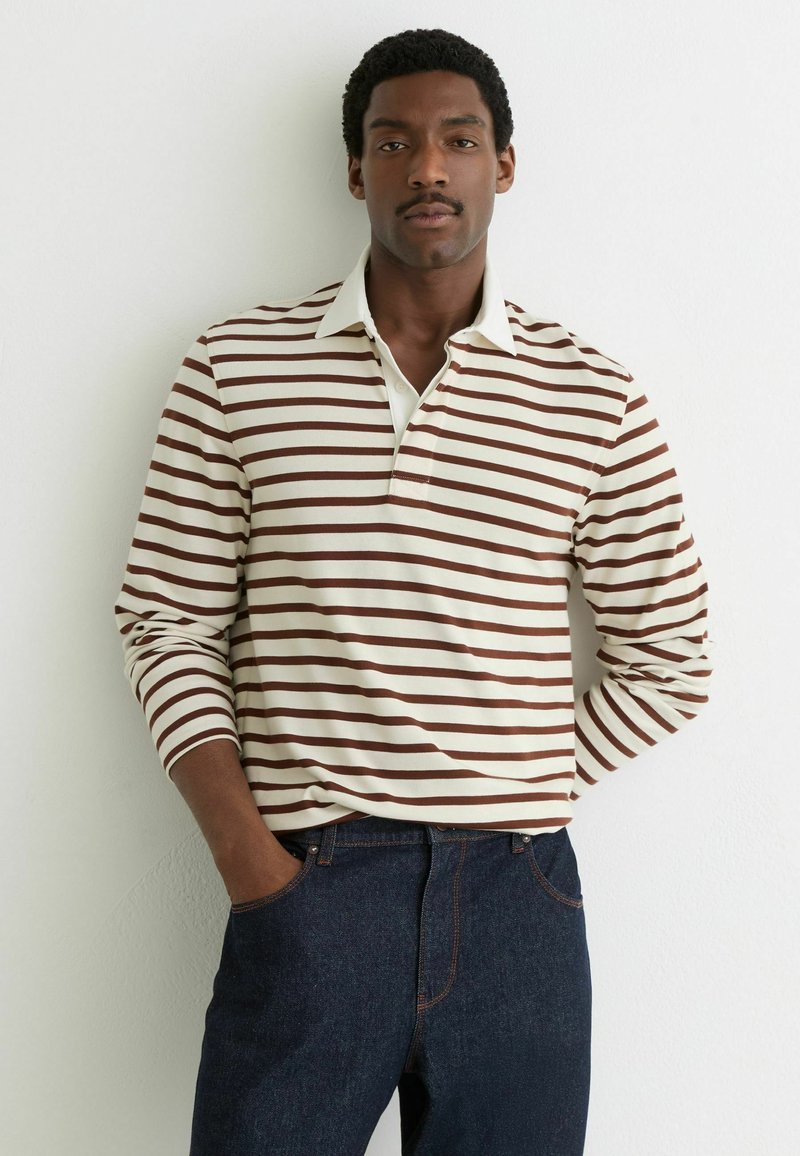 Koszulka polo w paski z długim rękawem w kolorze kremowo-brązowym, z kołnierzykiem i dopasowanym krojem. Dopasowana do ciemnoniebieskich dżinsów.