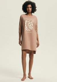 Jasnobrązowa bawełniana sukienka o luźnym kroju, z rękawami o długości trzy czwarte i roślinnym nadrukiem graficznym, z wysokim przodem i dłuższym tyłem oraz miękką teksturą.