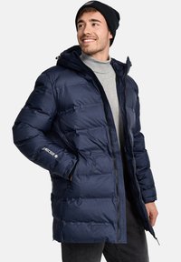 Chaqueta acolchada azul marino con cierre delantero, capucha y bolsillos laterales; fabricada con tela acolchada y resistente al agua; presenta un logo en la manga.