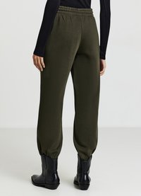 Pantaloni jogger verde oliva con vita elasticizzata, polsini affusolati e una texture morbida, abbinati a stivaletti neri alla caviglia.