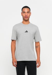 Sivá bavlnená tričko s kruhovým výstrihom a krátkymi rukávmi. Má malú čiernu adidas logo na hrudi. Hladká textúra, voľný strih.