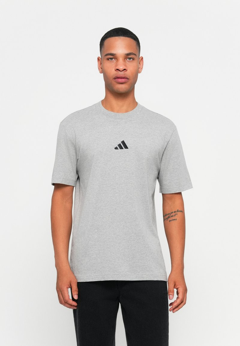 Siva bombažna majica z okroglim ovratnikom in kratkimi rokavi. Ima majhen črn adidas logotip na prsih. Gladka tekstura, sproščen kroj.