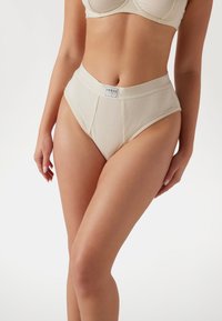 Tejfehér csíkozott, magas derekú alsónemű széles elasztikus derékkal és egy kis márkacímkével az elején. Minimalista dizájn, minta nélkül.