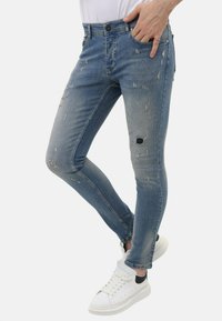 Verglaasde blauwe skinny jeans met versleten details, waaronder scheuren en rafelige randen. Gepaard met witte sneakers voor een casual look.
