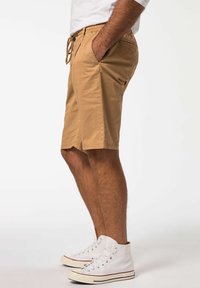 Brune bomuldsshorts med elastisk talje og snørelukning, med sidelommer og lige pasform, parret med hvide høj-top sneakers.