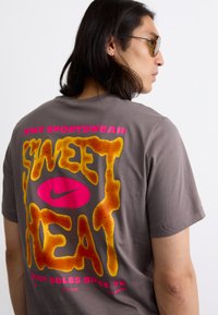 Grå bomuld t-shirt med et stort multifarvet grafik på ryggen. Teksten lyder "SWEET HEAT" og har orange og pink accenter.