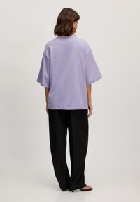 Light purple oversized t-shirt with short sleeves, soft fabric, and a relaxed fit, paired with black wide-leg pants.