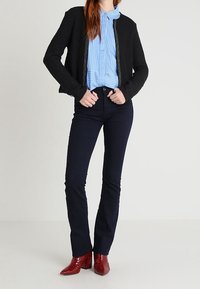 Černá bomber bunda, modrá a bílá pruhovaná košile s límcem, tmavé džíny a červené kotníkové boty na podpatku. Texturovaná tkanina a přiléhavý střih.