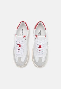 Sneaker bianchi con accenti rossi, dettagli in suede grigio e lacci bianchi. Presentano una tomaia texture e un colletto imbottito per il comfort.