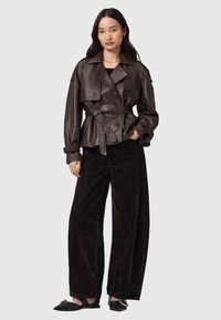 Palton din piele maro, cu centură, cu o siluetă ajustată, guler mare și închidere cu nasturi; asortat cu pantaloni largi din cording negru.