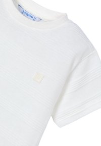 T-shirt bianco a maniche corte con strisce orizzontali texture, collo rotondo e un piccolo logo quadrato nella parte inferiore sinistra.