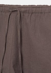 Pantalon en lin marron avec taille élastique et détail de lien sur le côté, présenté sur un fond uni.