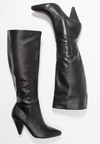 Ein Paar schwarze Lederstiefel bis zum Knie mit spitzen Zehen, Kegelabsätzen und seitlichen Reißverschlüssen an einem Stiefel.