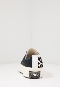 Czarno-biały nisko wycięty sneaker Converse z motywem lamparta na obcasie, widoczne logo na podeszwie z tyłu.