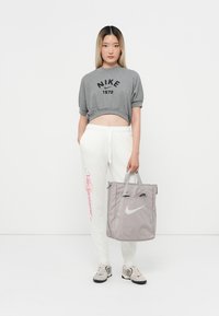 Harmaa lyhythihaisessa Nike-paidassa on musta logo, valkoisissa verkkareissa on vaaleanpunaista tekstiä, harmaassa kassi on valkoinen swoosh ja harmaissa lenkkareissa.