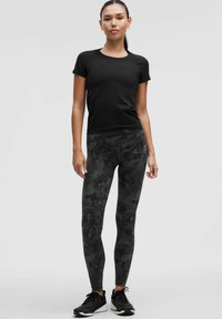 Musta urheilupaita lyhyillä hihoilla yhdistettynä korkeavyötäröisiin leggingseihin, joissa on tumma kukkametsästyskuvio. Mustat lenkkitossut viimeistelevät asun.