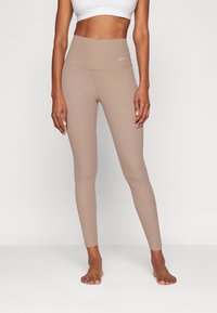 Leggings beige côtelés avec une taille haute et un discret logo, fabriqués dans un tissu extensible pour le confort et la flexibilité.