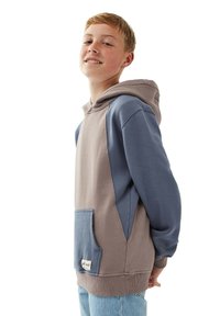 Huppari beigen ja sinisten sävyjen yhdistelmässä, jossa on etutasku, ribattu helma ja teksturoitu kangas rentoa istuvuutta varten.