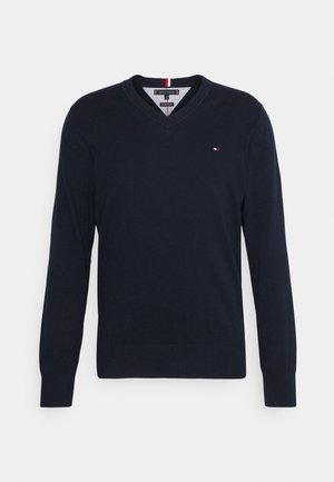 Pull bleu marine à col en V, manches longues et petit logo rouge, blanc et bleu sur la poitrine gauche.