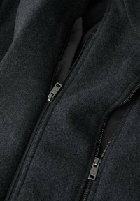 Chaqueta gris oscuro con un exterior suave y texturizado de lana, doble cremallera y forro negro. Vista en primer plano que resalta la costura y el detalle de la cremallera.