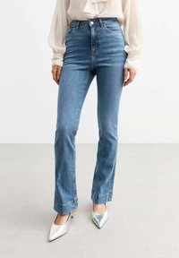 Lichtblauwe high-waisted jeans met een slim fit en een lichte flare bij de enkels, voorzien van klassieke stiksels en zakken, gecombineerd met zilveren hakken.